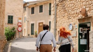 People walk down a quaint, stone-walled street.