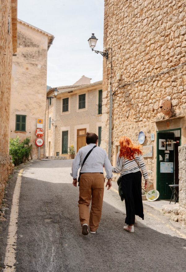 People walk down a quaint, stone-walled street.